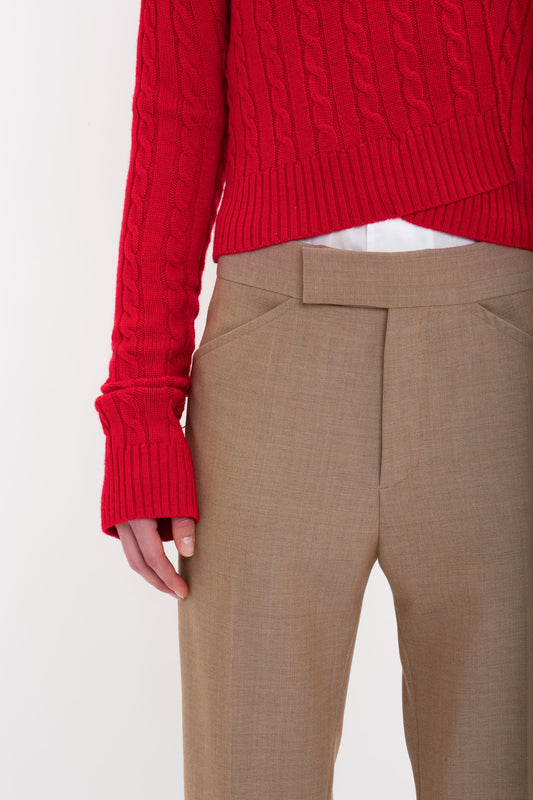 Person wearing a red cable-knit sweater and beige, 1970s-inspired Victoria Beckham Wide Cropped Flare Trouser In Tobacco with kick hem, showcasing a partial view of the hands and torso.