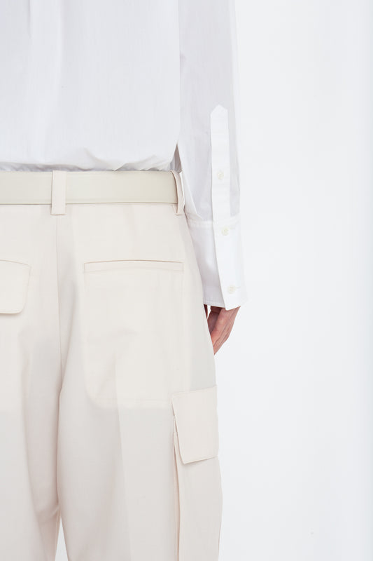 Back view of a person wearing a white shirt tucked into Victoria Beckham's Relaxed Cargo Trouser In Bone with a relaxed silhouette and a white belt. Two pockets are visible on the trousers along with a side cargo pocket. The outfit is crafted from 100% cotton for ultimate comfort.