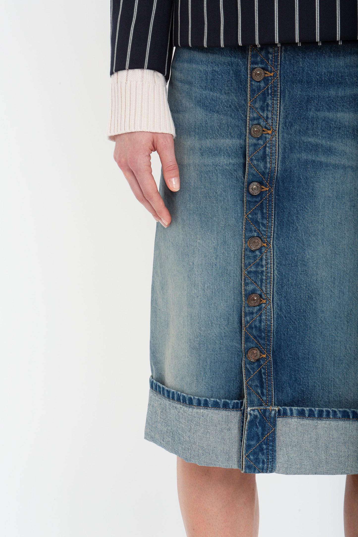 A person wearing the Victoria Beckham Placket Detail Denim Skirt In Heavy Vintage Indigo Wash paired with a long-sleeved top featuring white cuffs.