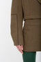 Close-up of a person wearing a brown coat of merino wool and a Victoria Beckham Tailored Mini Skirt In Khaki. Only the lower half of the coat and the upper part of the skirt are visible along with one hand touching the coat's pocket.