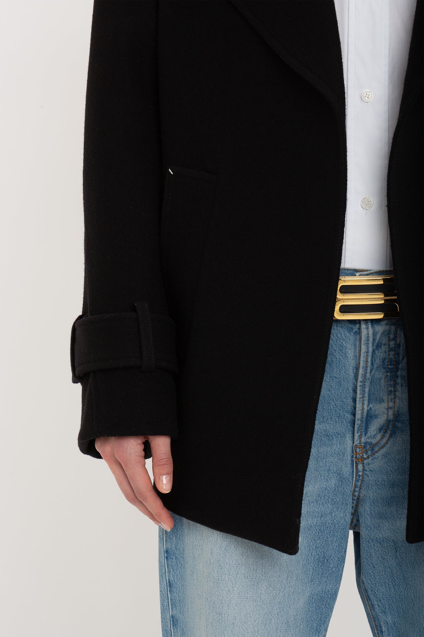 Person wearing a Victoria Beckham Oversized Pea Coat In Black over a white shirt with blue jeans and a black and gold belt with a rectangular buckle.