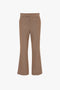 A pair of Victoria Beckham Wide Cropped Flare Trouser In Tobacco with a slight flare at the bottom and front pleats, reminiscent of classic 1970s-inspired trousers.