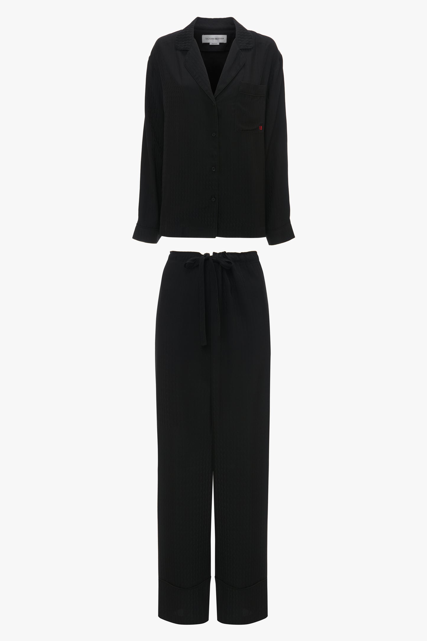 A black two-piece outfit, the VB Monogram Pyjama Sleep Set In Black from Victoria Beckham, crafted from 100% silk pyjama fabric, including a long-sleeved, button-up top and high-waisted, drawstring pants.