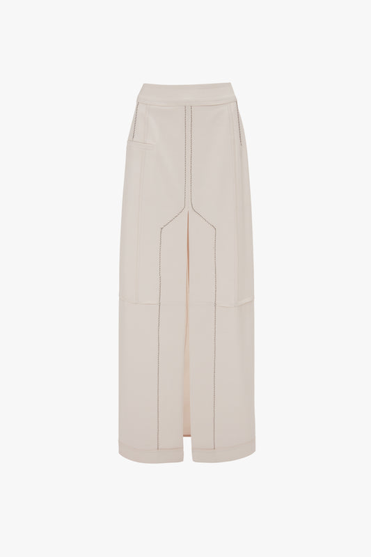 A white, high-waisted floor-length skirt with black stitching and two front pockets. The Deconstructed Floor-Length Skirt In Bone by Victoria Beckham features an exposed central front seam detail, a box pleat detail, and a small slit at the front hem.