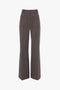 A pair of high-waisted, wide-leg trousers in a brown and white checkered pattern, featuring front pockets and belt loops. These Victoria Beckham Alina Trousers in Tobacco are perfect for any stylish wardrobe.