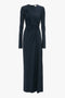 A long-sleeve, floor-length navy blue dress with a ruched detail on one side and a round neckline, reminiscent of the Victoria Beckham Ruched Detail Floor-Length Gown In Midnight.