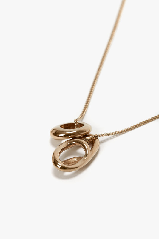 Exquisitely crafted in Italy, the Victoria Beckham Exclusive Abstract Charm Necklace In Light Gold features two interlocking oval pendants on a thin gold chain, set against a white background.