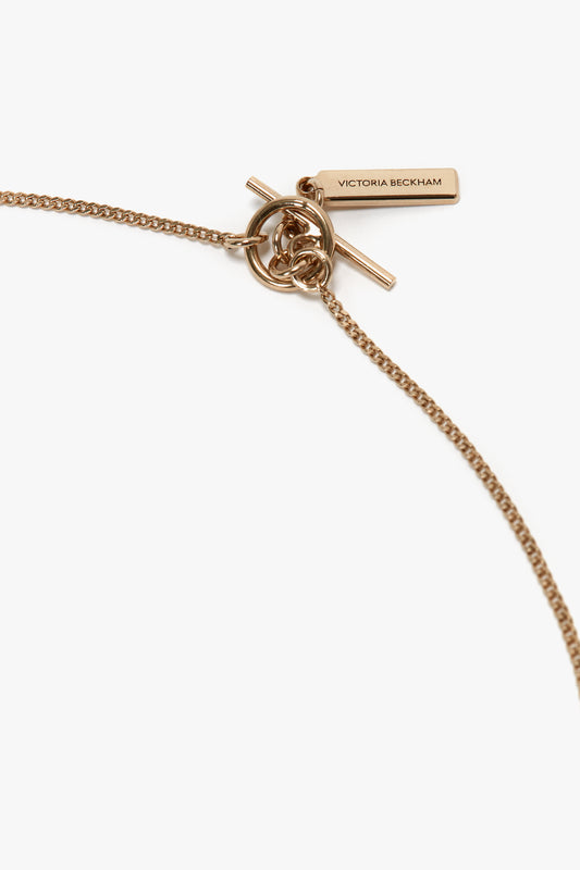 Exclusive Abstract Charm Necklace In Light Gold with a circular knot and an abstract charm, featuring a rectangular tag inscribed "Victoria Beckham," exquisitely crafted in Italy.