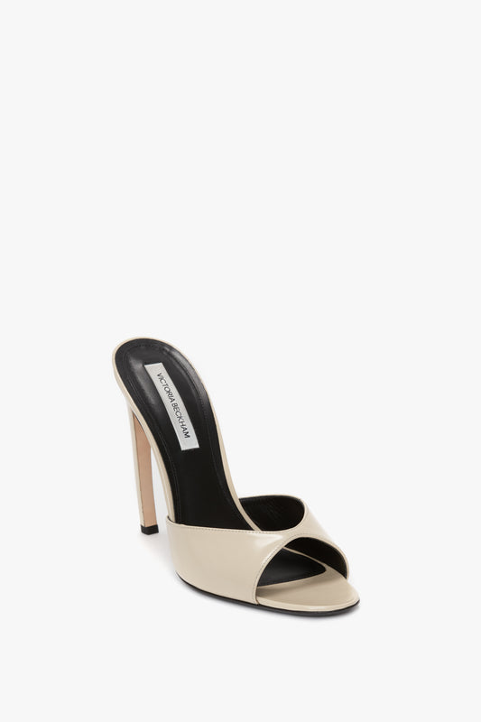 A single beige Classic Mule In Macadamia calf Leather by Victoria Beckham with an open toe, black insole, and a seductive curved heel, crafted from luxury calf leather, is positioned against a white background.