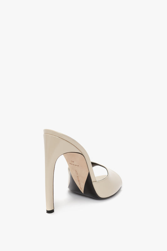 A beige high-heeled women's shoe made from luxury calf leather, featuring an open back, a seductive curved heel, and an arch strap, viewed from the rear angle on a white background. Product Name: Classic Mule In Macadamia calf Leather Brand Name: Victoria Beckham