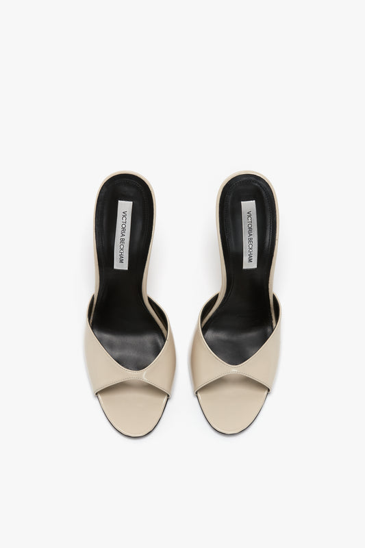 A pair of **Classic Mule In Macadamia calf Leather by Victoria Beckham** with black insoles, featuring a cross-strap design and branded insoles, offering flattering toe cleavage.