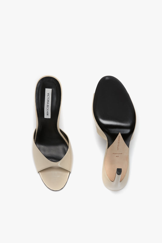 A pair of beige and black Classic Mule In Macadamia calf Leather with leather soles, one shoe facing upward to reveal the insole with a Victoria Beckham brand label and V cut detail, and the other showing the luxury calf leather sole with size and material details.