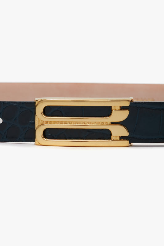 Close-up of the Victoria Beckham Frame Belt In Midnight Blue Croc Embossed Calf Leather with gold hardware and buckle, featuring a croc-embossed calf leather strap in Midnight Blue and a brown interior.
