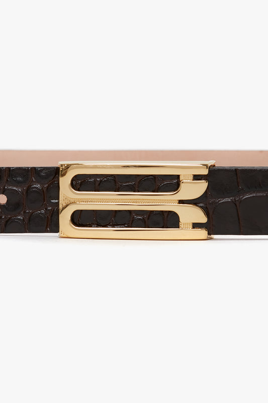 Close-up of a **Victoria Beckham Frame Belt In Espresso Croc Embossed Calf Leather**, featuring a gold double-pronged buckle set against an alligator skin texture.