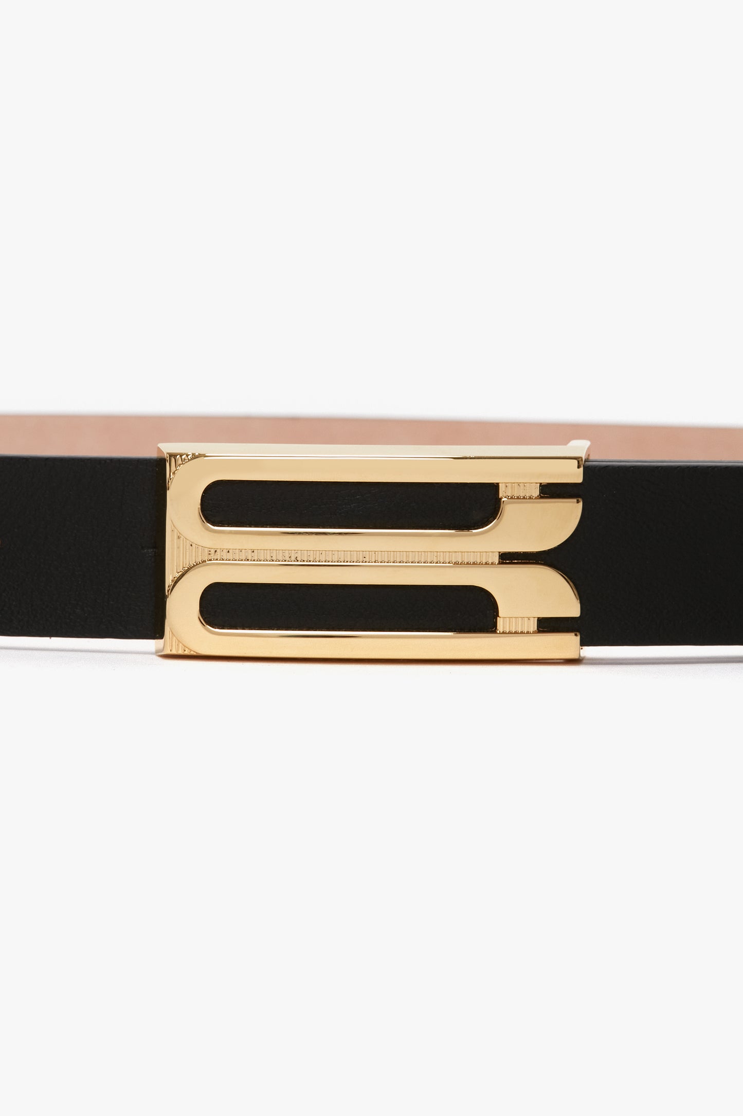 A versatile accessory, the Victoria Beckham Frame Belt In Black Leather with a gold rectangular buckle featuring two parallel cut-out lines in the center is a wardrobe classic.