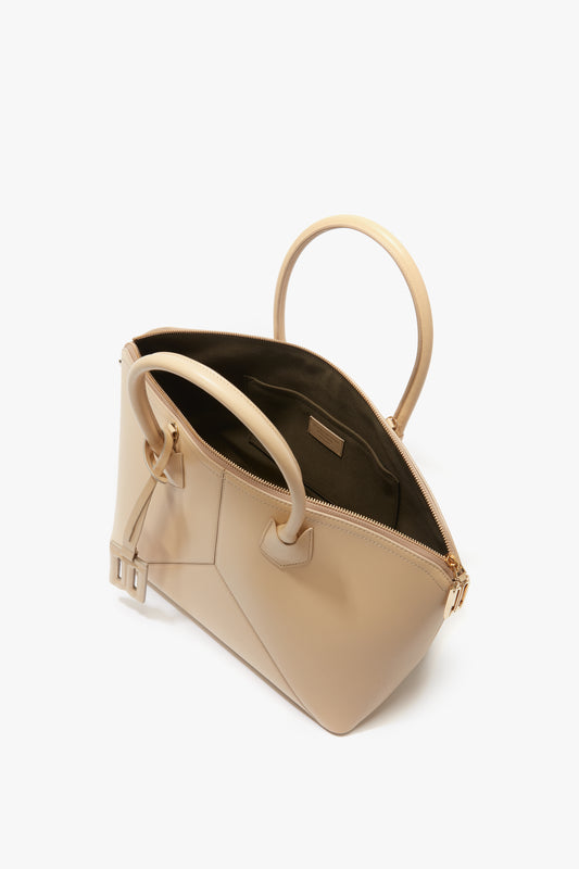 A tan leather **Victoria Bag In Sesame Leather by Victoria Beckham** with gold zippers, open to reveal its internal compartments and handle straps, accentuated by elegant leather panels and an adjustable strap for customized comfort.