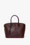 A Victoria Beckham Victoria Bag In Burgundy Leather with dual handles, a structured design, and a small tag attached.