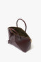 A Victoria Beckham Victoria Bag In Burgundy Leather with a gold zipper opens to reveal an olive green interior, featuring two top handles and an adjustable strap on the side.