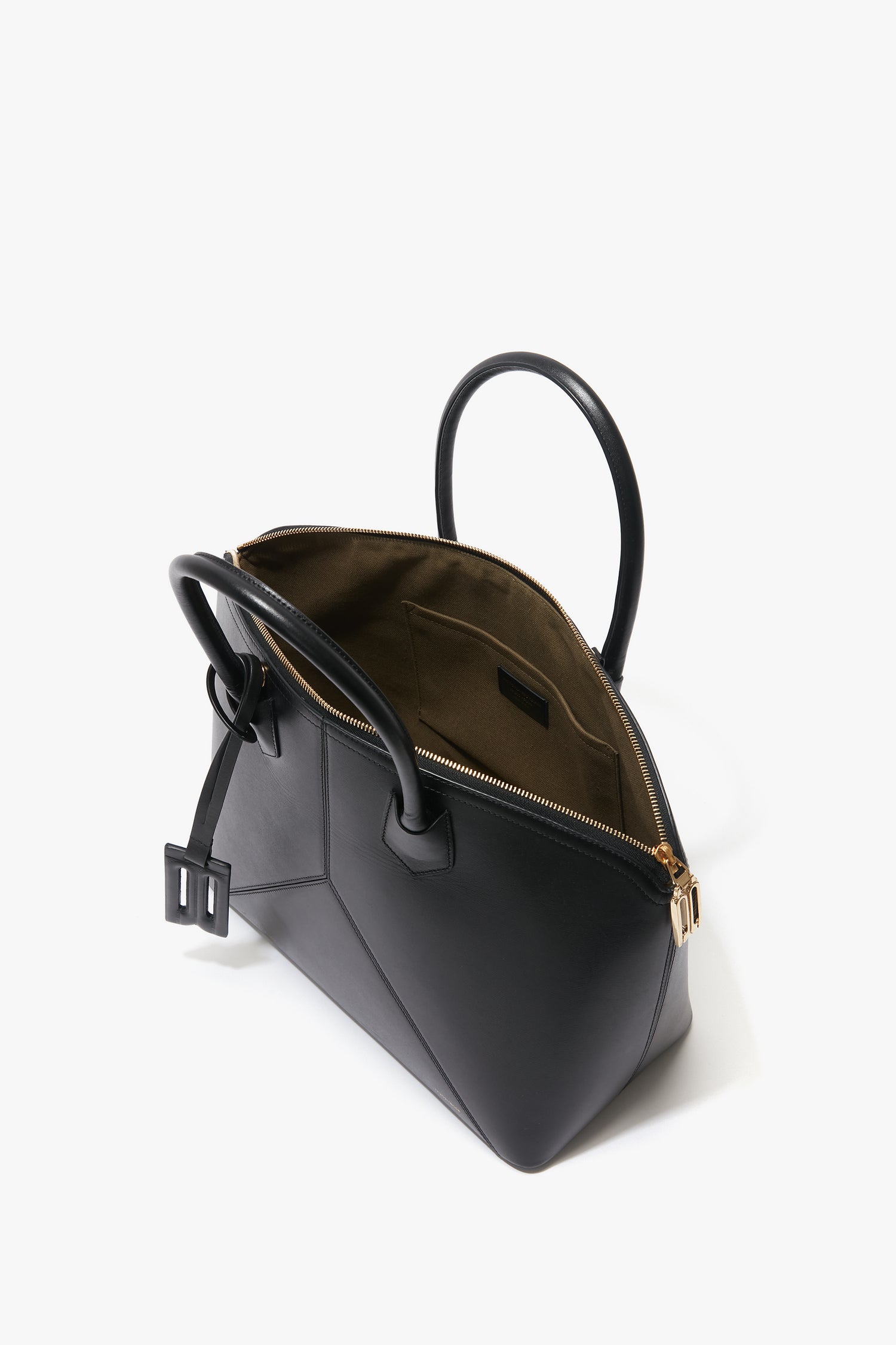 The Victoria Beckham Victoria Bag In Black Leather is a black leather handbag with gold hardware, unzipped to reveal a brown interior. Designed with versatile hold-all functionality, it boasts two black handles, leather panels, and a small attached belt.