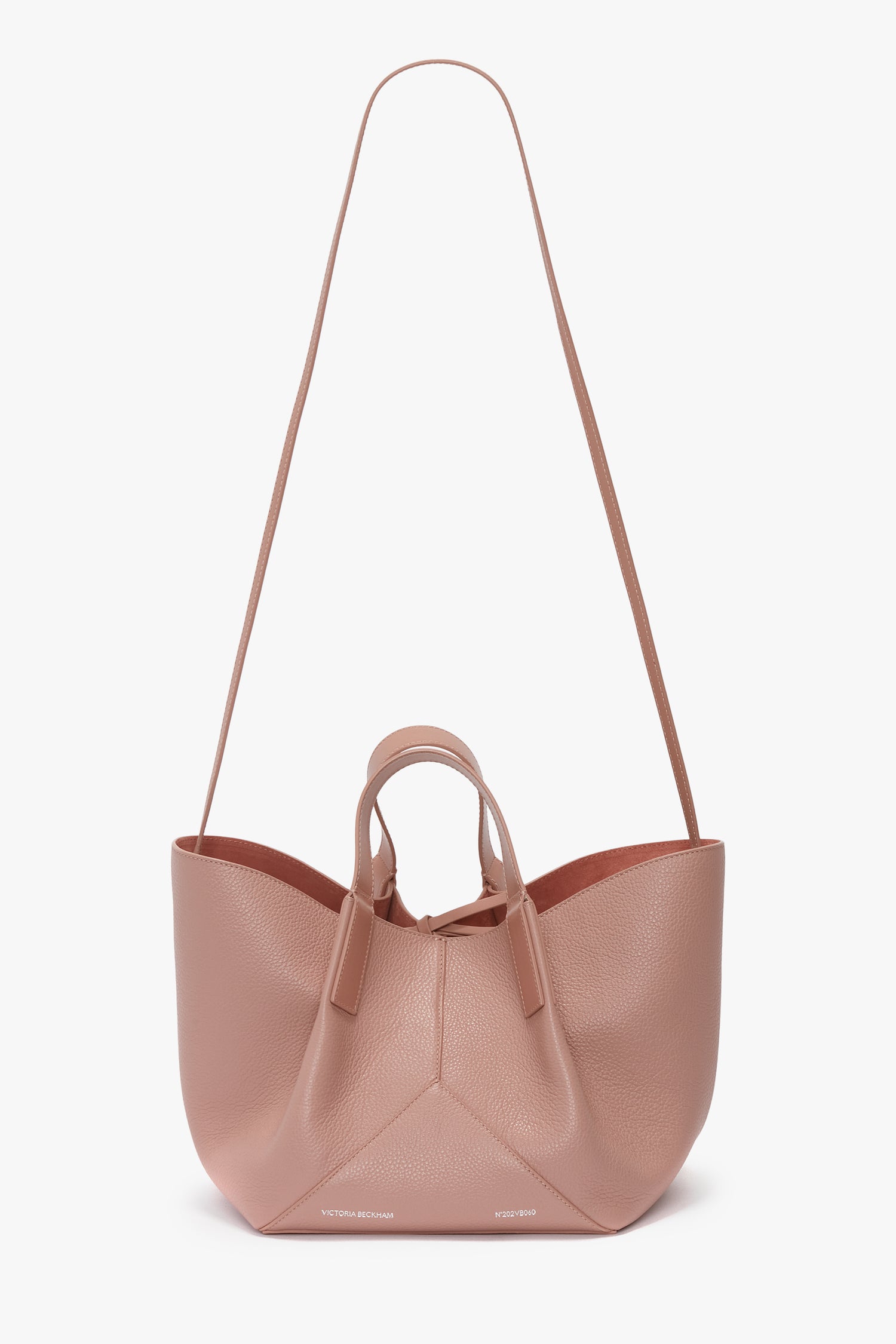 A pink mini tote bag crafted from luxurious calf leather, featuring a long shoulder strap and two short handles. The bag boasts a minimal design with a delightful marshmallow-pink hue and a textured finish.
The **W11 Mini Tote Bag In Marshmallow Leather** by **Victoria Beckham** boasts a minimal design with a delightful marshmallow-pink hue and a textured finish.