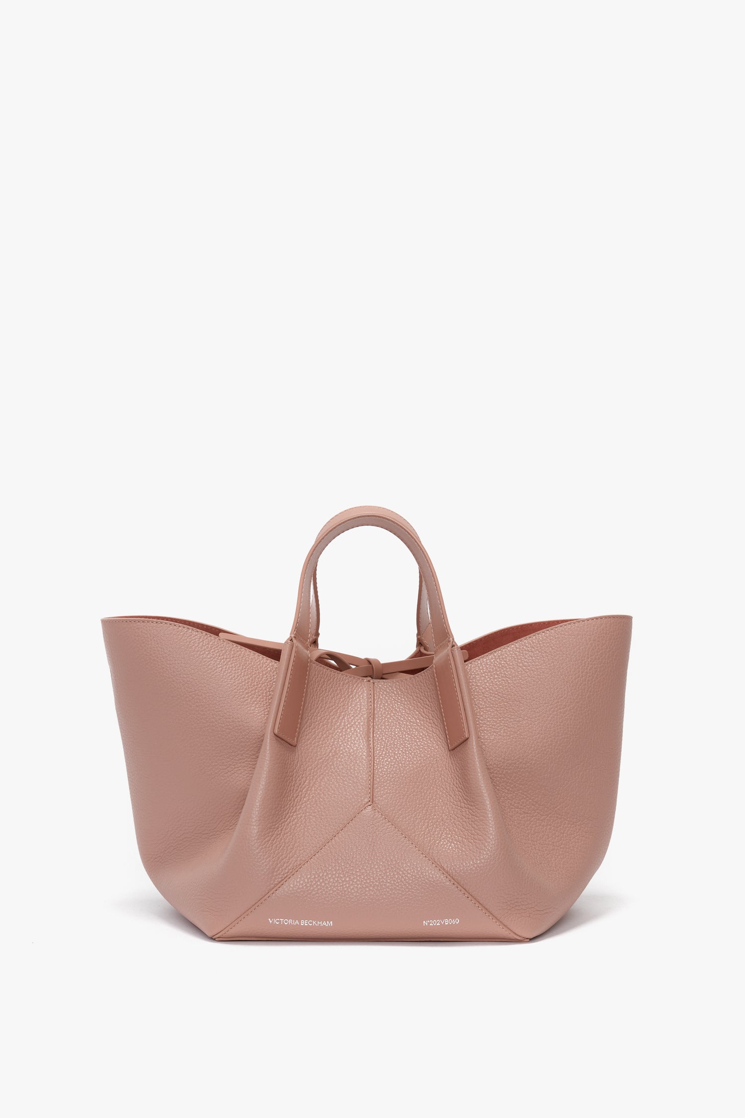 A large, blush pink mini tote bag crafted from calf leather with two handles, featuring subtle embossed text at the base. The W11 Mini Tote Bag In Marshmallow Leather by Victoria Beckham exudes elegance and quality.