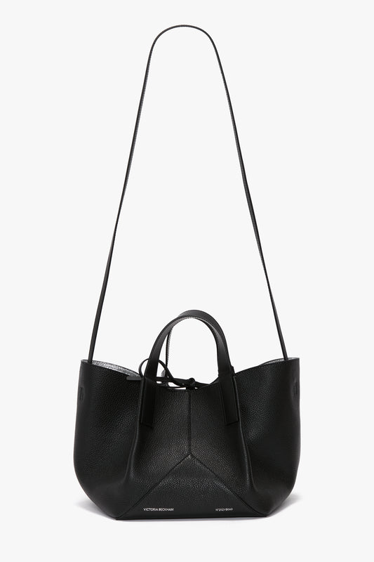 A W11 Mini Tote In Black Leather by Victoria Beckham with sophisticated leather handles and a long shoulder strap is displayed against a white background.