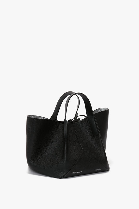 A W11 Mini Tote In Black Leather by Victoria Beckham with two looped leather handles, showcasing luxurious sophistication and a soft, unstructured shape, featuring subtle branding at the base.