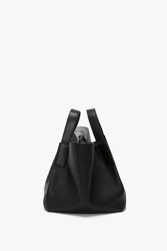 W11 Mini Tote In Black Leather by Victoria Beckham, with a simple, structured design, featuring luxurious sophistication and pebbled texture, complemented by two leather handles, set against a white background.