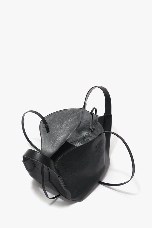 An open black leather handbag with a gray interior and multiple straps, featuring luxurious sophistication, is displayed against a plain white background has been replaced by the W11 Mini Tote In Black Leather by Victoria Beckham.