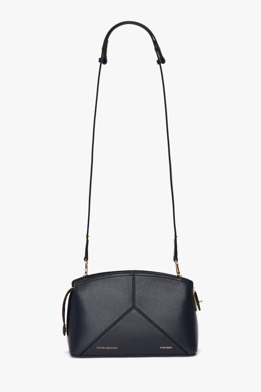 A navy leather crossbody bag with gold-toned hardware, featuring a geometric design on the front and an adjustable strap. The structured silhouette adds sophistication to this luxurious accessory. This is the Exclusive Victoria Crossbody Bag In Navy Leather by Victoria Beckham.