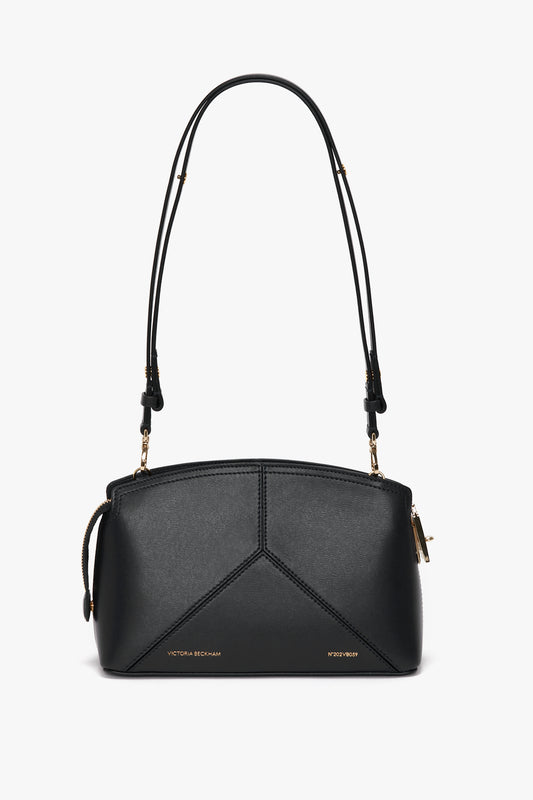 A Victoria Beckham Victoria Crossbody In Black Leather with a structured design, featuring gold hardware and an adjustable, removable strap. Crafted from textured calf leather, the brand name "Victoria Beckham" is printed near the bottom.