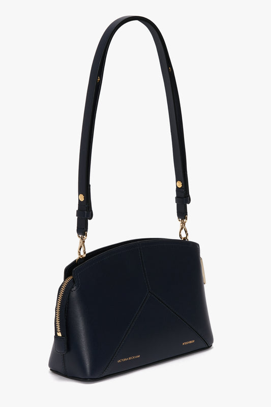 A navy leather handbag with gold hardware, featuring a structured silhouette, a single shoulder strap, and a zip closure. A branded padlock and the text "Victoria Beckham" are visible on the lower front.