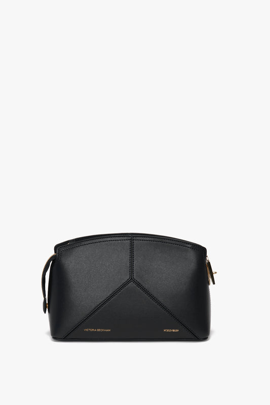The Victoria Crossbody In Black Leather, crafted from textured calf leather, features gold zippers and small gold branding text on the front, designed by Victoria Beckham. This stylish crossbody comes with an adjustable removable strap for added versatility.