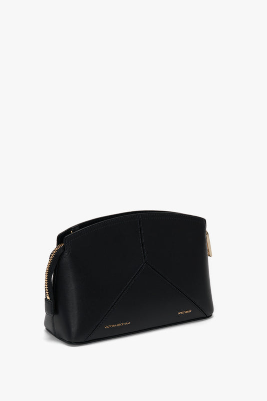 A Victoria Beckham Victoria Crossbody In Black Leather with a geometric design, gold zipper, and small gold text near the bottom, featuring an adjustable removable strap for versatile styling.
