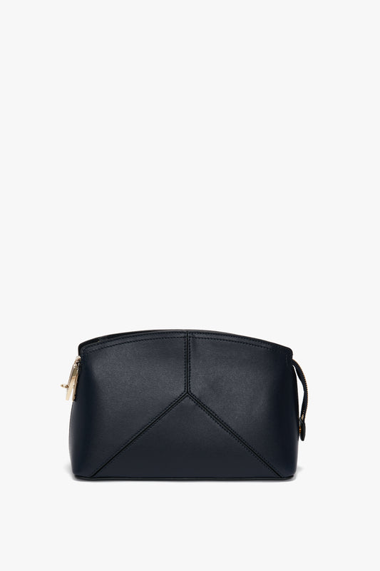 A small black leather handbag with a structured silhouette and minimalistic design, featuring gold-tone hardware, a branded padlock, and a zip closure has been replaced with the Exclusive Victoria Crossbody Bag In Navy Leather by Victoria Beckham.
