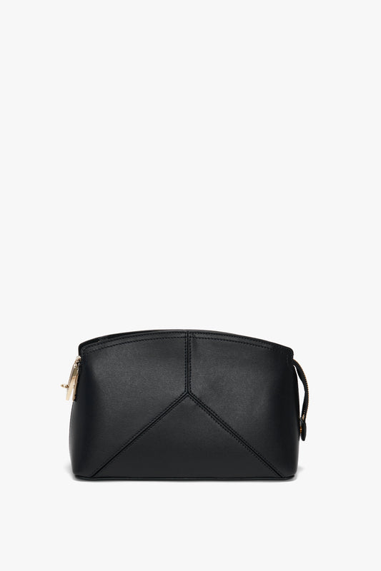 A small, black, structured handbag crafted from textured calf leather, featuring a geometric design at the front, gold zipper closure, and a thin handle. This **Victoria Beckham Victoria Crossbody In Black Leather** comes with an adjustable removable strap.