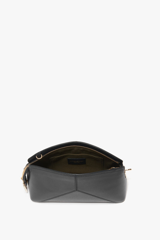 Black leather handbag with a zippered opening, showing an empty interior lined in green fabric. Crafted from textured calf leather, this chic Victoria Crossbody In Black Leather by Victoria Beckham also features an adjustable removable strap for versatile wear.