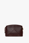 A small, dark brown calf leather clutch bag with a sleek design, featuring subtle stitching and gold zipper accents. The text "Victoria Beckham" and "Victoria Crossbody Bag In Burgundy Leather" is printed on the front, complemented by a stylish padlock closure.