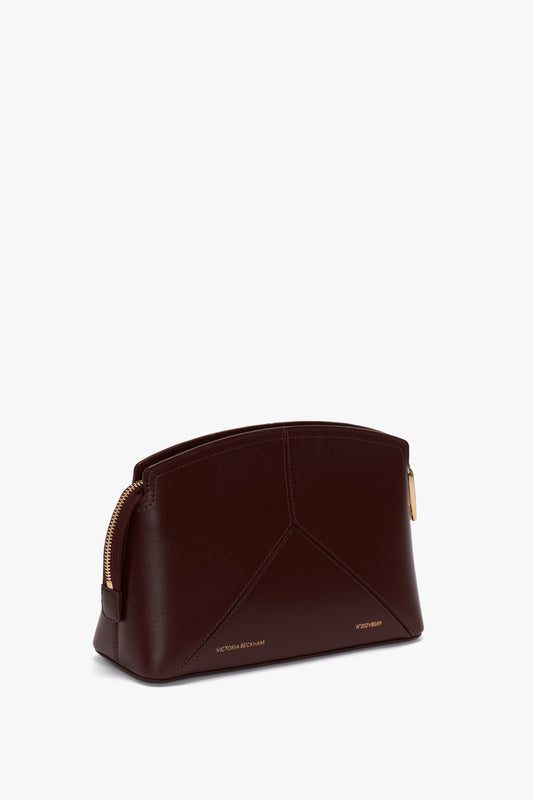 A Victoria Crossbody Bag In Burgundy Leather with gold zippers and embossed text at the bottom, featuring "Victoria Beckham," complete with a sleek padlock closure for added security.