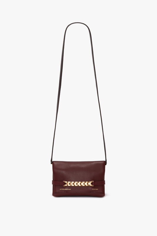 A Victoria Beckham Mini Chain Pouch Bag With Long Strap In Burgundy Leather, featuring a thin black strap and gold-tone chain detail on the front.