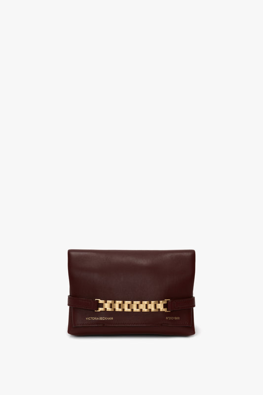 A maroon clutch with a gold-tone chain detail on the front. The words "Victoria Beckham" are printed on the bottom left, making this Mini Chain Pouch Bag With Long Strap In Burgundy Leather a stylish accessory.