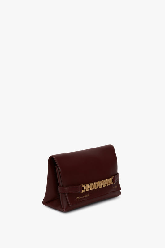 A Mini Chain Pouch Bag With Long Strap In Burgundy Leather with a gold-tone chain detail on the front displays the brand name "Victoria Beckham" in elegant gold lettering at the bottom.