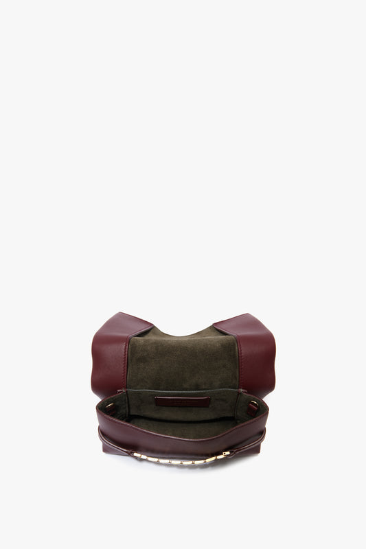 Open Victoria Beckham Mini Chain Pouch Bag With Long Strap In Burgundy Leather with dark green interior and gold-tone chain detail, revealing an empty main compartment and a small inner pocket against a plain white background.