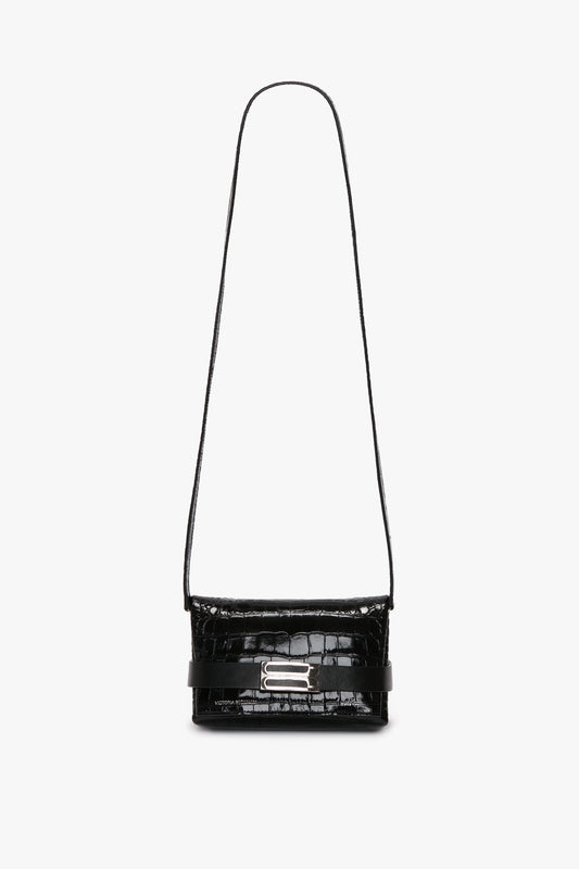 A black calf leather crossbody bag with an embossed crocodile print, a long strap, and a silver buckle on the front. The Mini B Pouch Bag In Croc Effect Black Leather by Victoria Beckham.