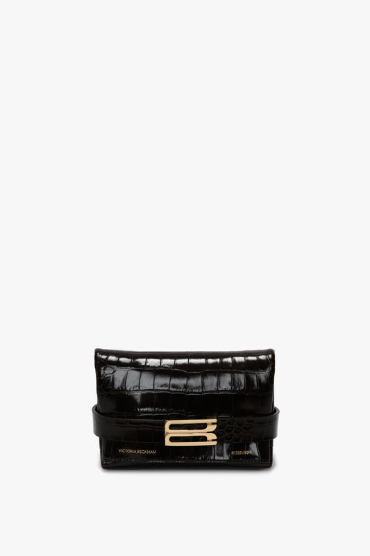A Mini B Pouch Bag In Croc Effect Espresso Leather with a gold rectangular buckle in the center, featuring "Victoria Beckham" embossed in gold on the front and a detachable crossbody strap for versatile styling.