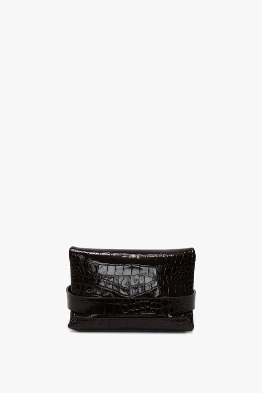 A black crocodile-embossed clutch bag made from calf leather, featuring a structured rectangular shape and a detachable crossbody strap, shown on a white background has been replaced with the Mini B Pouch Bag In Croc Effect Espresso Leather by Victoria Beckham.