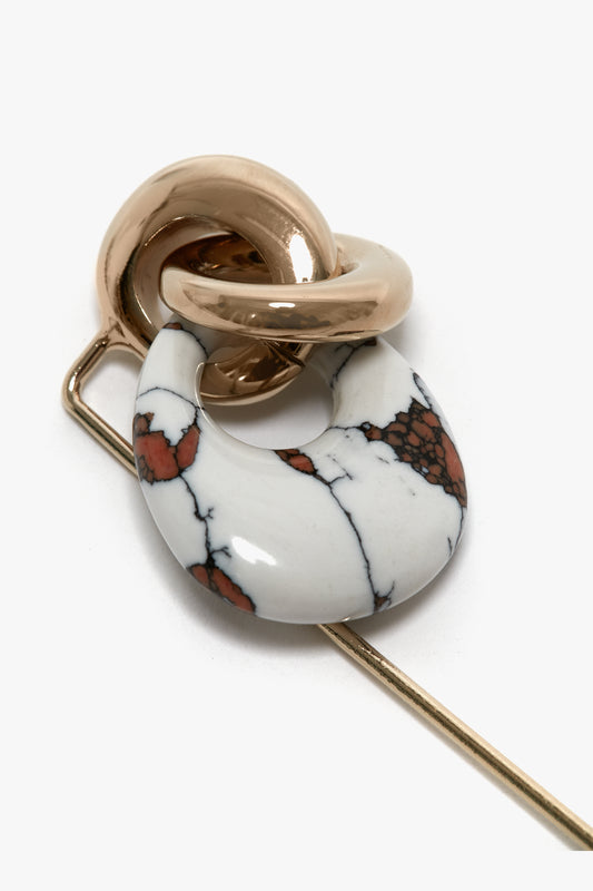 Close-up of an Exclusive Resin Charm Brooch In Light Gold-White by Victoria Beckham featuring interlocking light gold and white marble-patterned stone loops, meticulously crafted and made in Italy, all attached to a sleek straight metal pin.