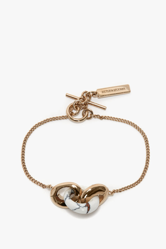 Exclusive Resin Charm Bracelet In Light Gold-White with a white marbled knot centerpiece and a toggle clasp featuring a rectangular tag engraved with "Victoria Beckham." This adjustable bracelet seamlessly blends elegance and versatility.