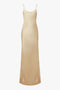 A long, silky beige slip dress with thin spaghetti straps and a smooth, form-fitting silhouette, reminiscent of a 1990s-inspired dress crafted from luxurious crepe back satin has been replaced by the Exclusive Floor-Length Cami Dress In Gold by Victoria Beckham.