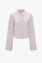 A Victoria Beckham Button Detail Cropped Shirt In Rose Quartz, featuring long sleeves, a pointed collar, and a front pocket, is displayed against a white background.